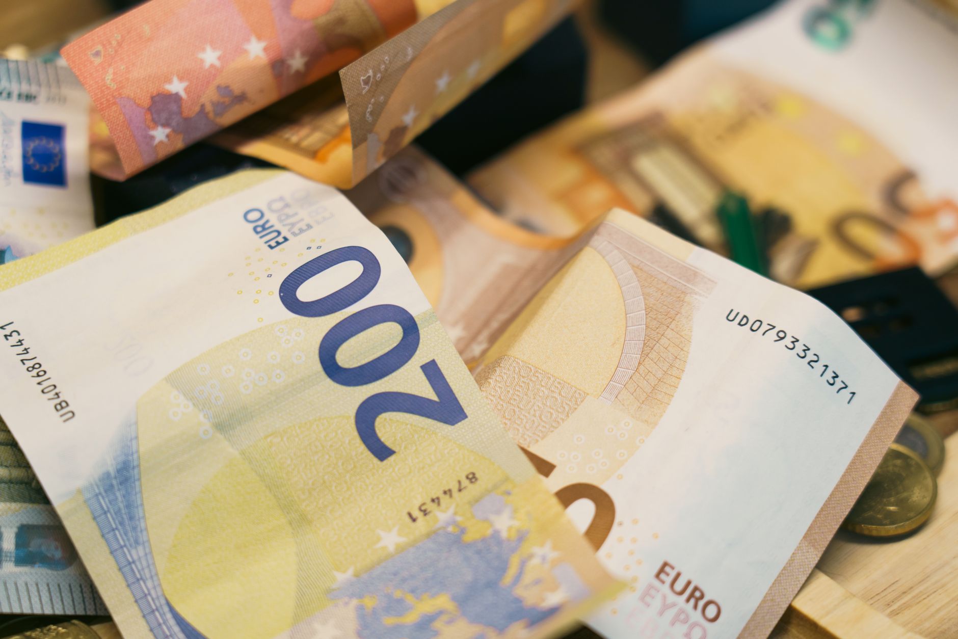 Notas de euro e de real brasileiro dispostas sobre uma mesa de madeira ao lado de uma calculadora