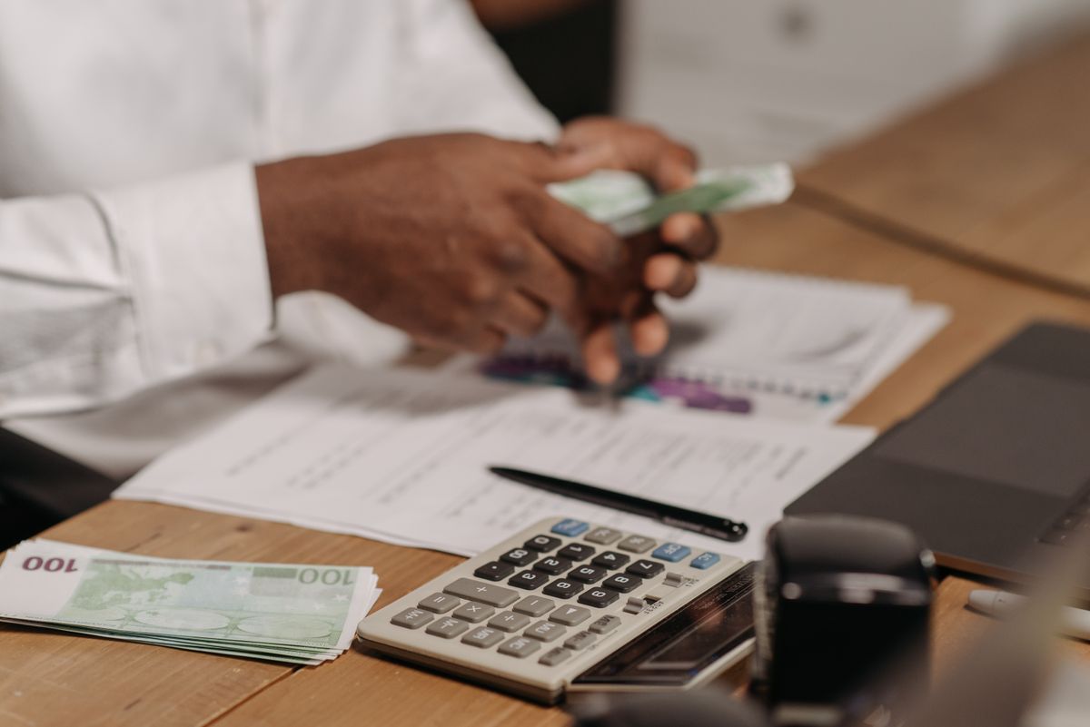 Pessoa analisando contrato de financiamento em euro e usando laptop ao lado de cédulas de moeda europeia.