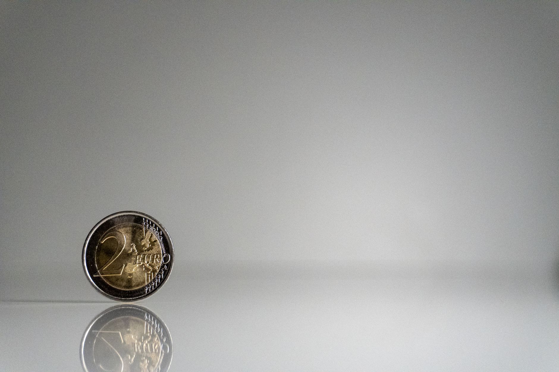 Como Investir na Europa Morando no Brasil: Guia Prático A minimalist image of a 2 euro coin with reflection on a sleek surface.
