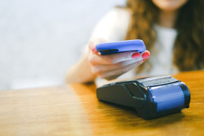 Close-up of a woman making a contactless payment using a smartphone over a card reader