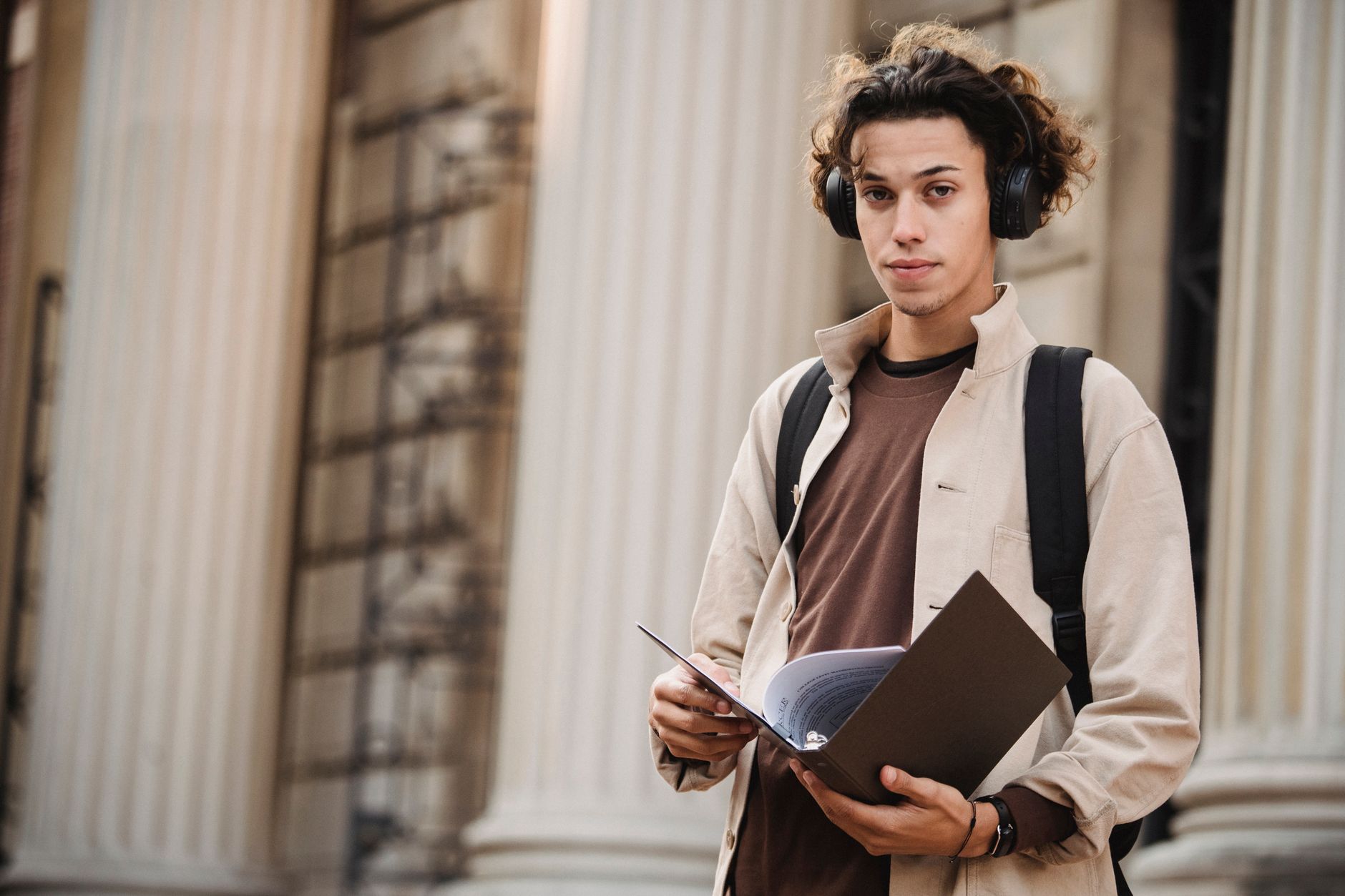Estudante com mochila e passaporte consultando aplicativo no celular em um campus europeu.