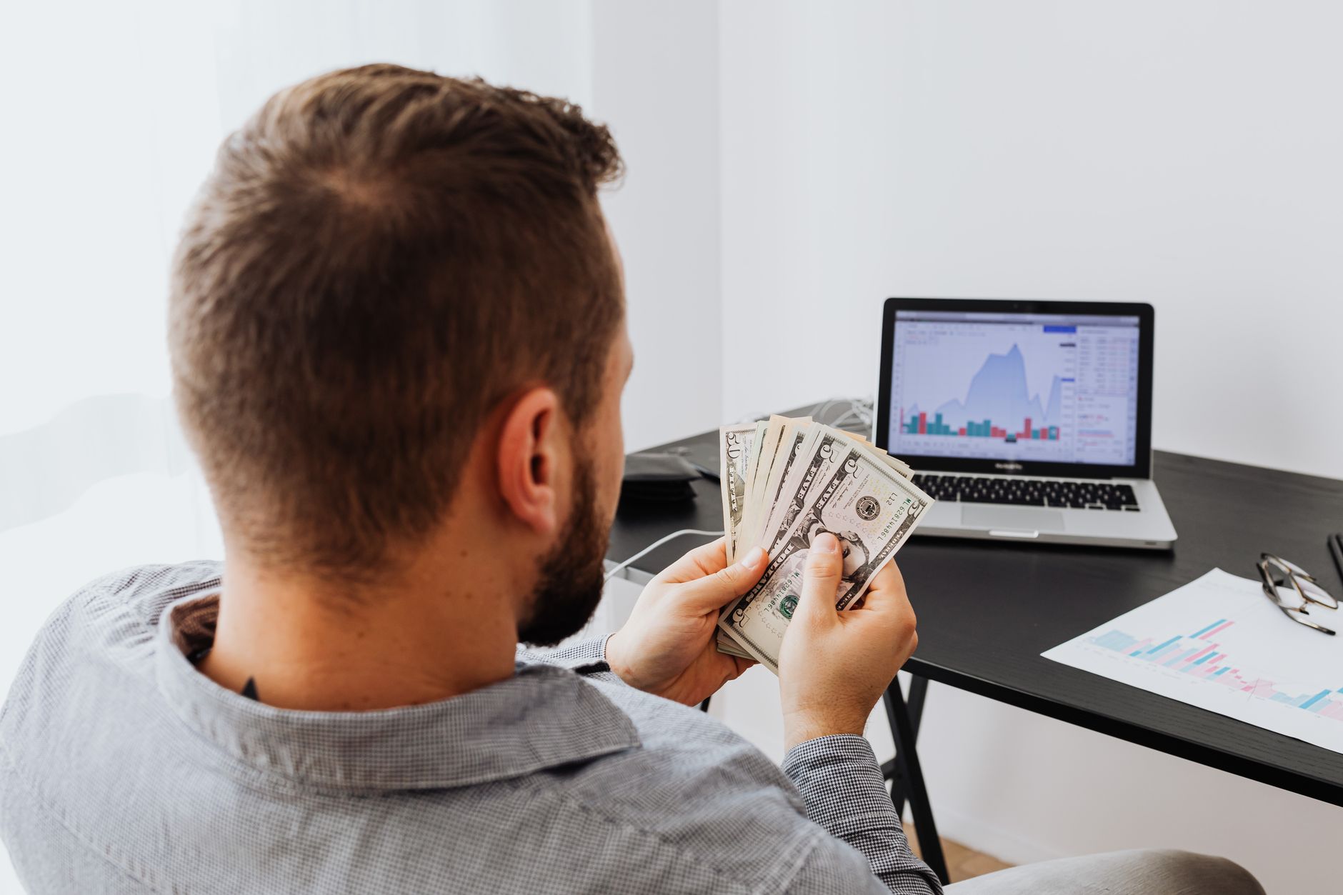 Pessoa analisando cotações de euro, dólar e real em uma mesa de trabalho