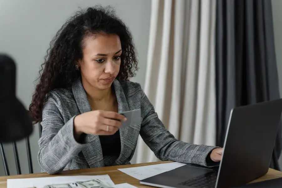 Mulher na mesa de trabalho com cartão de crédito, notebook e dinheiro, concentrada Mulher na mesa de trabalho com cartão de crédito, notebook e dinheiro, concentrada