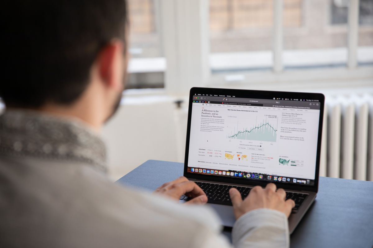 Pessoa analisando gráficos de cotação cambial em um laptop sobre uma mesa de escritório.