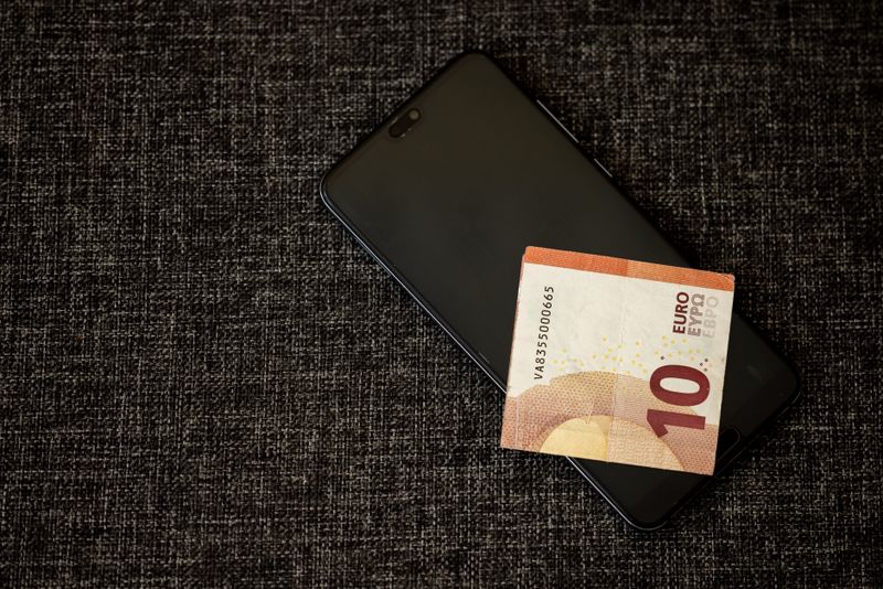 Fundo Cambial ou ETF de Dólar: Qual a Melhor Opção Simples? A 10 euro banknote placed on a smartphone on a textured dark fabric background.