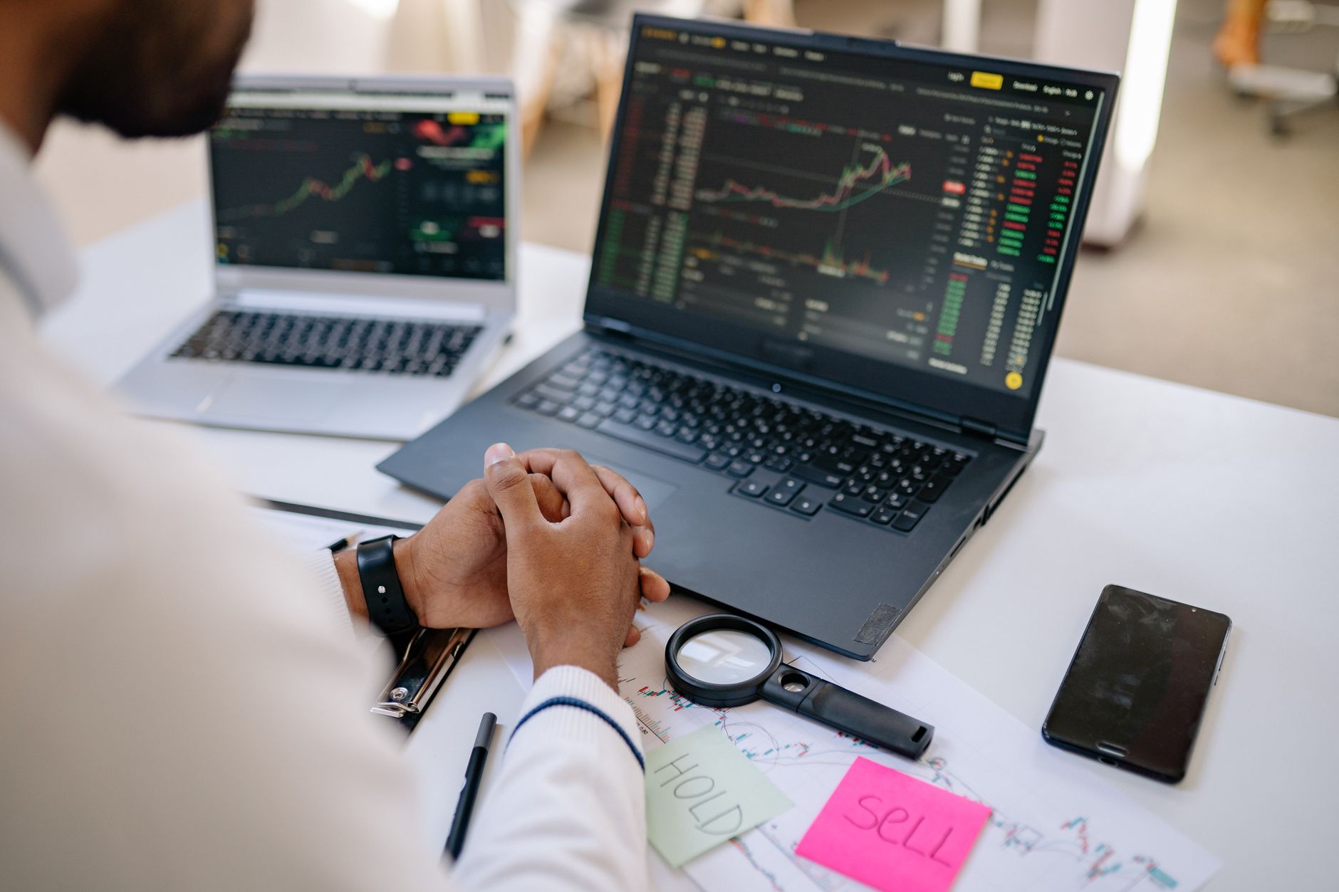 Pessoa analisando gráficos financeiros e cotações da moeda europeia em um computador portátil sobre uma mesa de madeira.