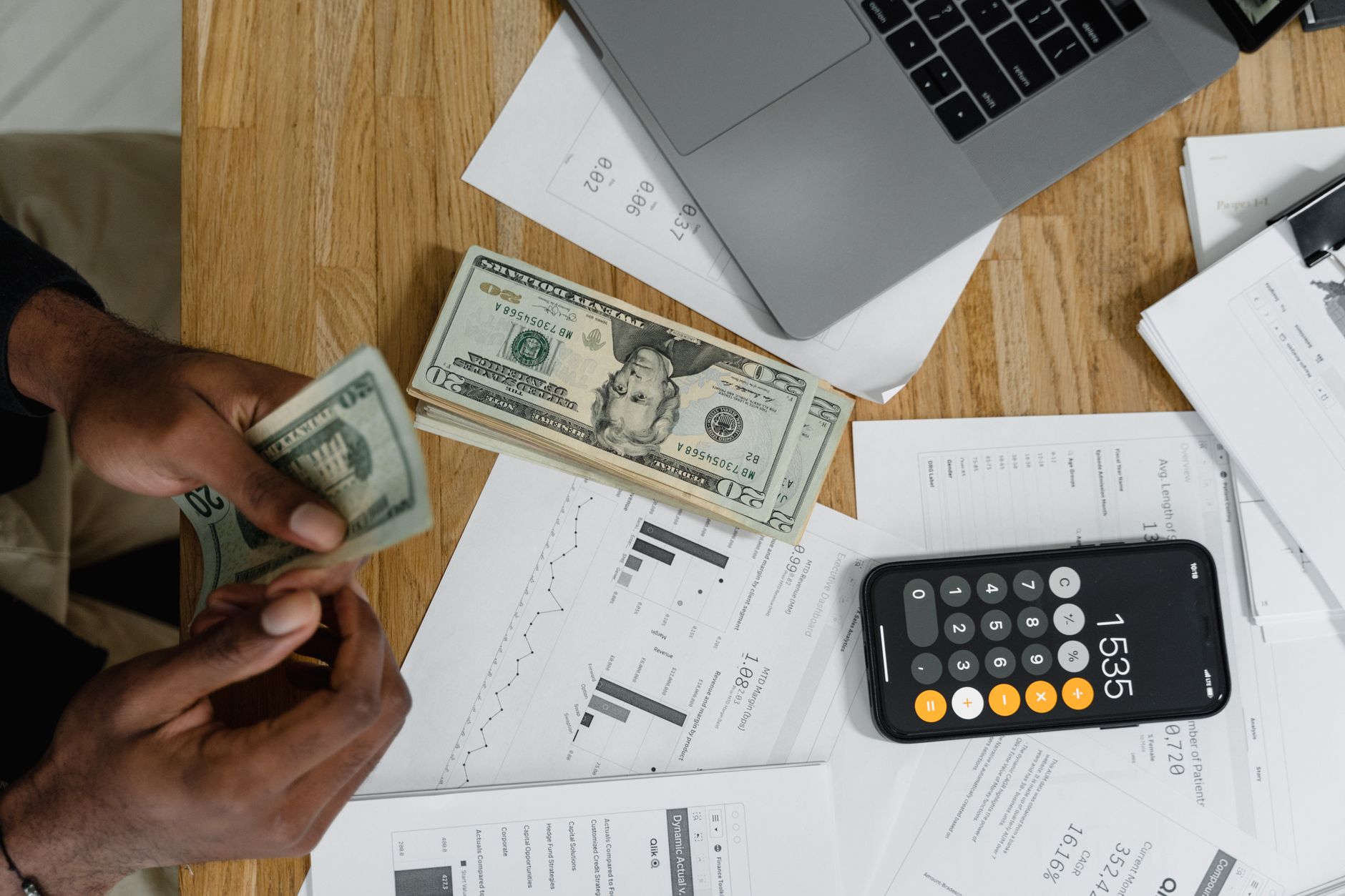 Histórico do dólar: principais altas e quedas Close-up of hands counting cash on desk with calculator, charts, and laptop, illustrating financial management.