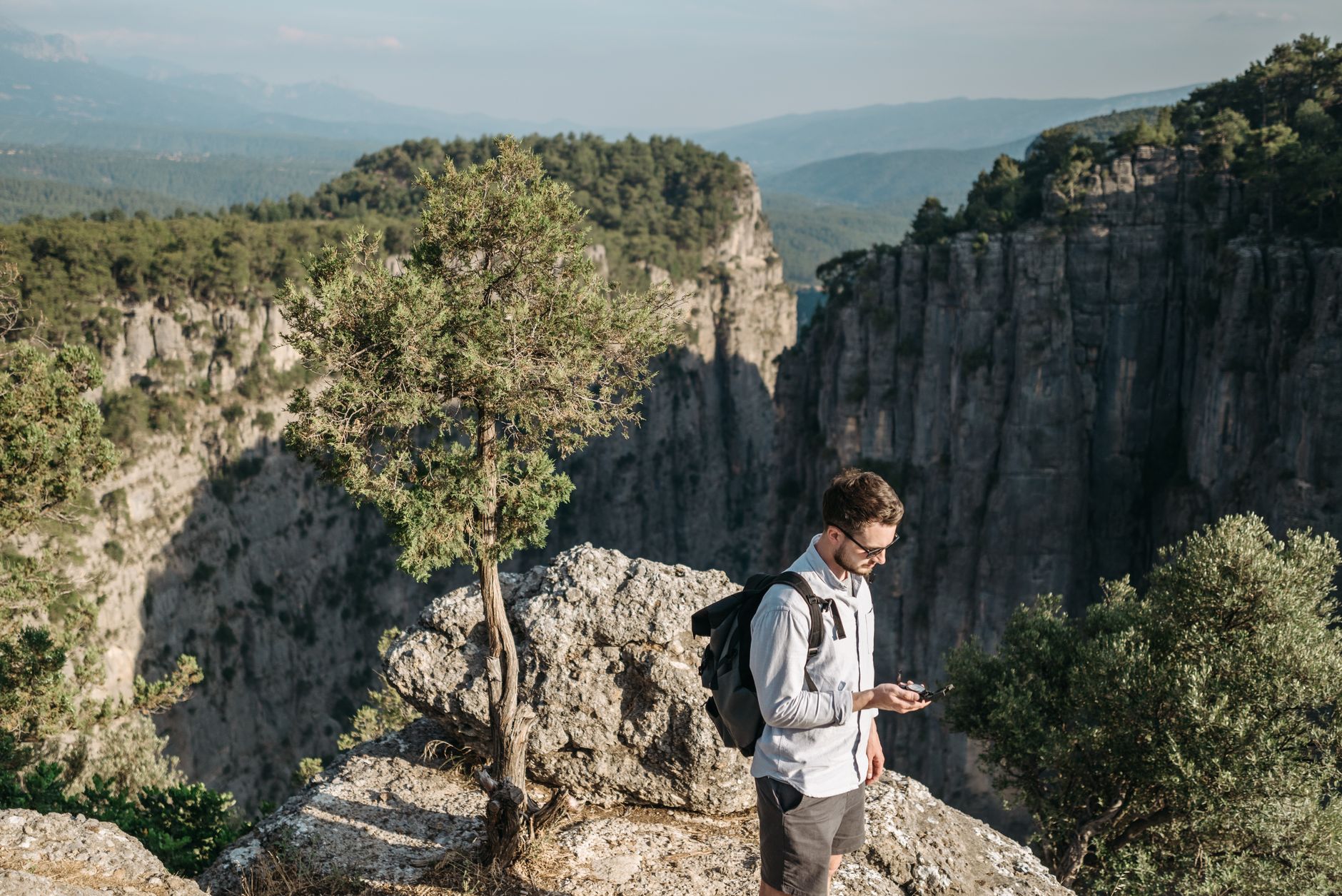 Quais impostos existem na compra de euro? A young man with a backpack uses a smartphone for navigation in a breathtaking canyon landscape.