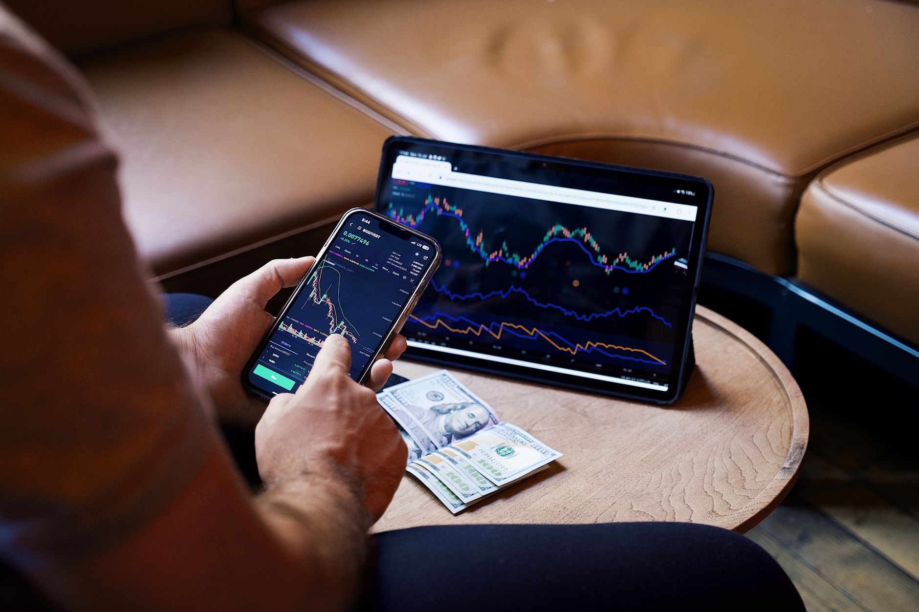 Pessoa segurando cédulas de euro em frente a um gráfico de cotação financeira em um computador.