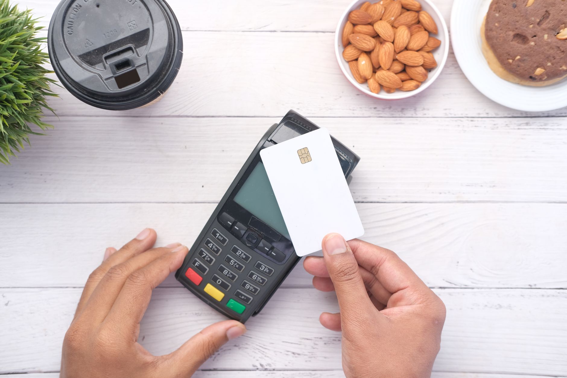 Inter Gold internacional: vale a pena para viajar? Hands making a contactless payment with a credit card on a wooden table.