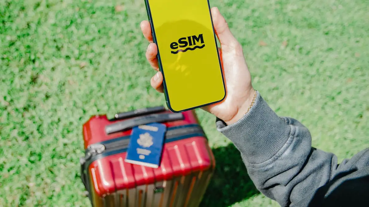 Viajante segurando smartphone com eSIM ao lado de mala vermelha
