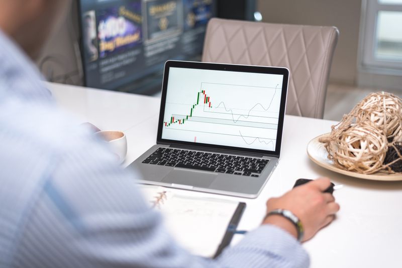 Ouro ou dólar: quando usar o metal na proteção cambial Man reviewing financial analysis on laptop in a modern office setting with focus on trading charts and data.