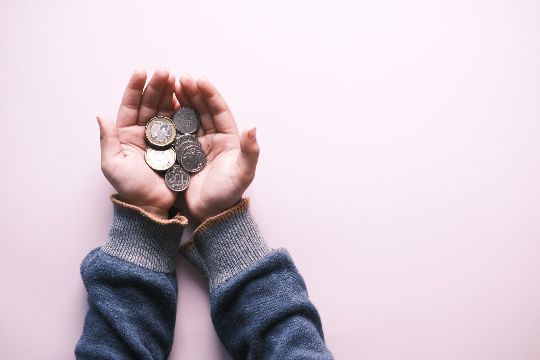 IOF sobre Euro em Espécie: Entenda a Tributação na Compra Close-up of hands in sweater holding various coins, indicating savings and finance on a white background.
