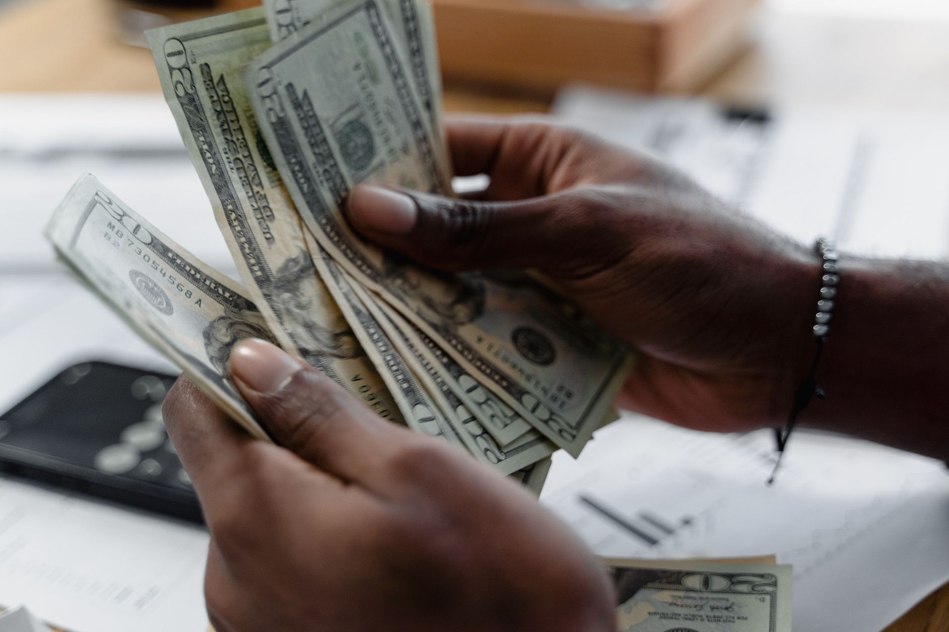 Como as diferenças de juros entre EUA e Europa afetam o euro Detailed image of hands counting US dollar bills on a desk, emphasizing finance and budgeting.