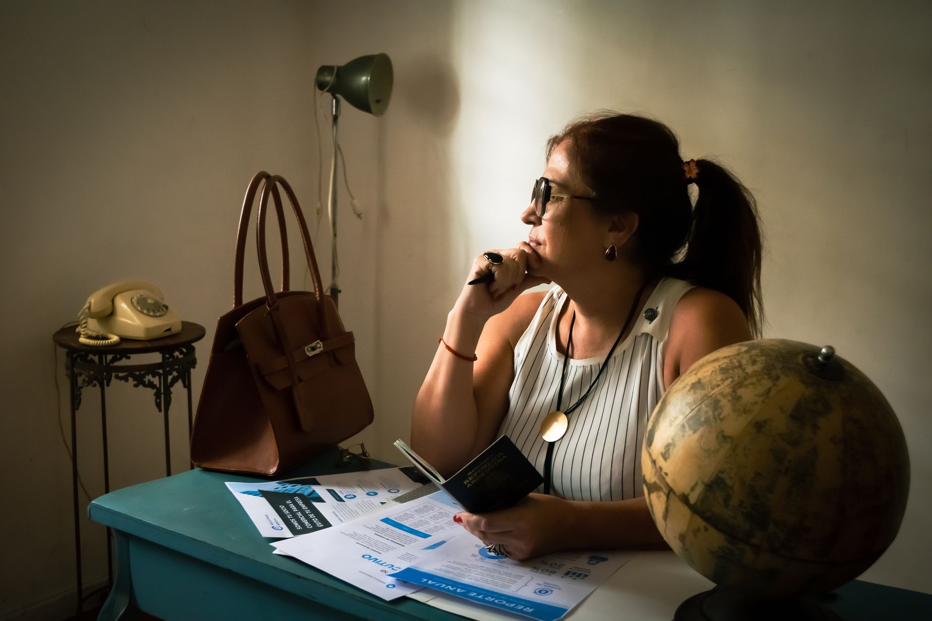 Levar dólar para os EUA: quando é obrigatório declarar A woman in a vintage office contemplating with a globe, documents, and classic phone.