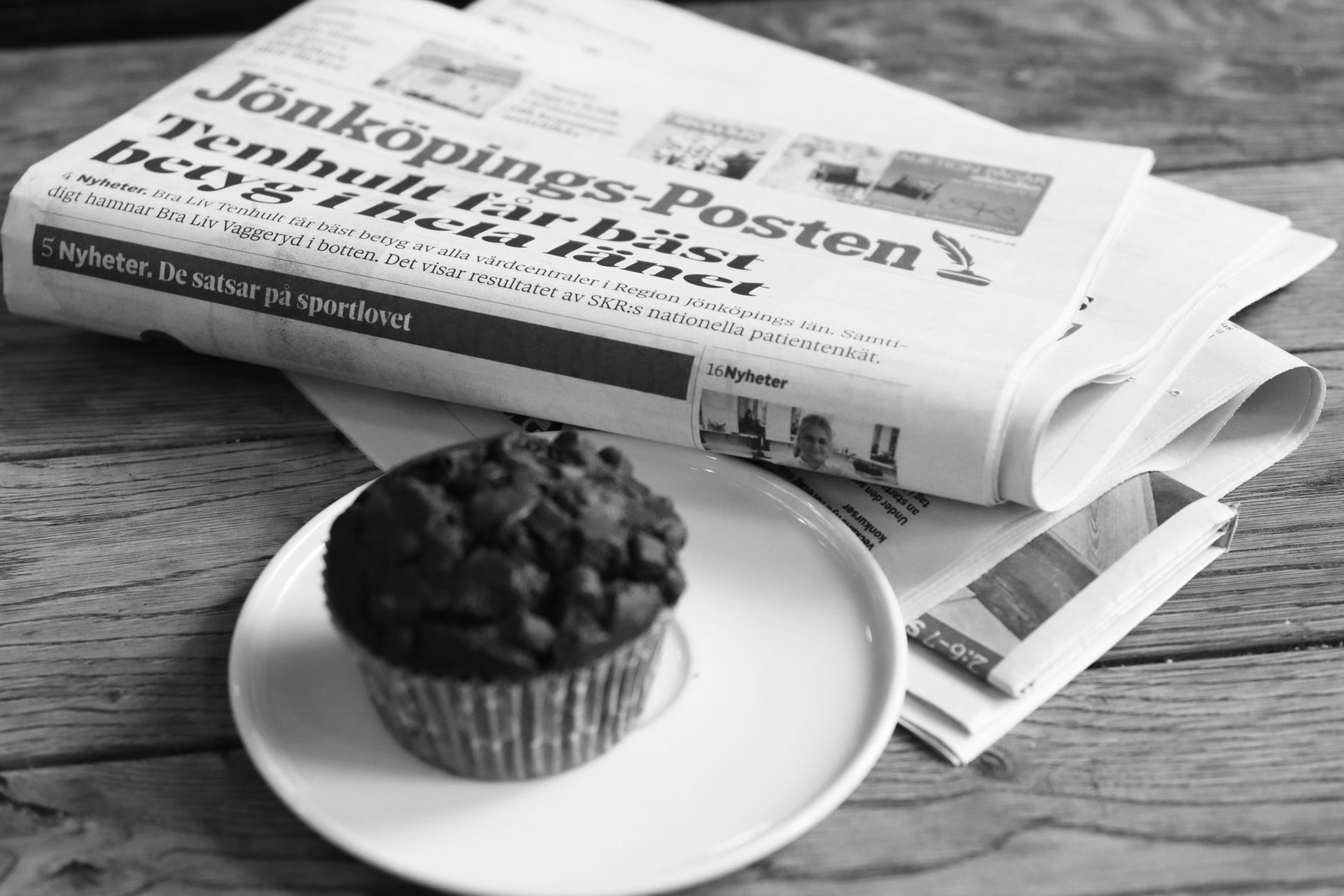 Black and white photo of Jönköpings-Posten and a chocolate muffin on a table.