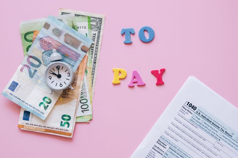 O que é risco cambial e como ele aparece no seu extrato Flat lay of taxes, currency, and reminder to pay on pink background.