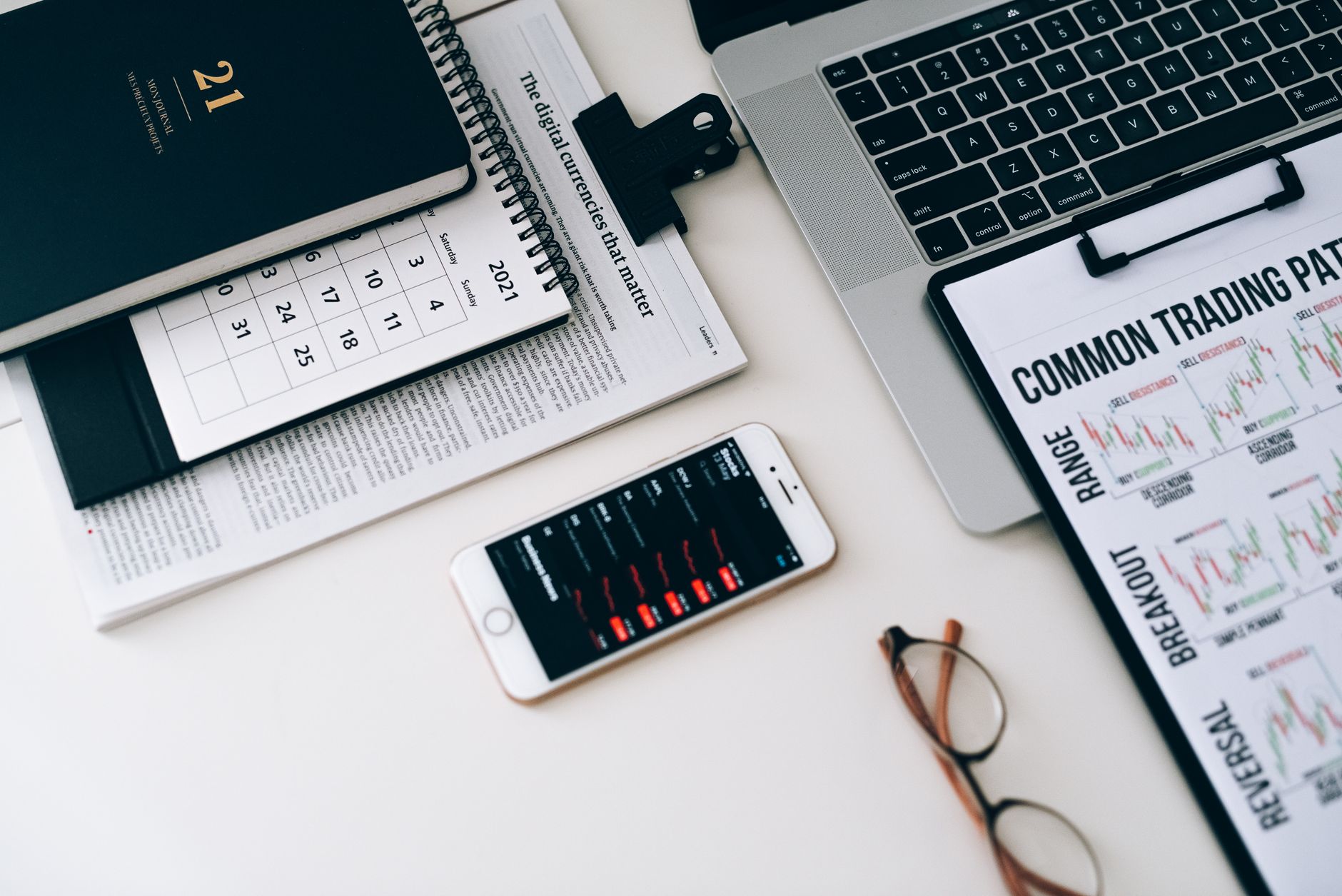 Home office desk featuring trading charts, smartphone, and laptop for financial analysis.