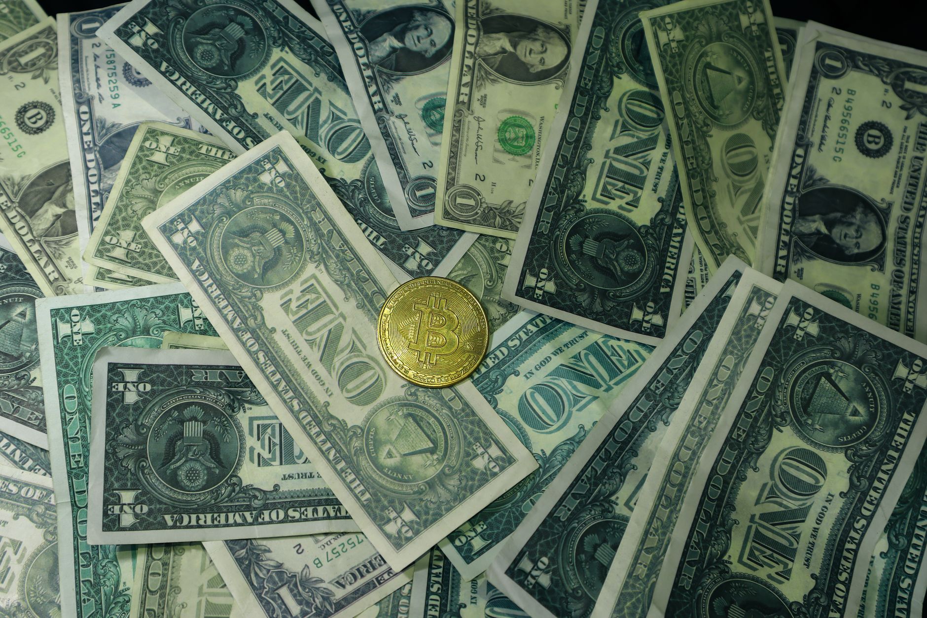 A golden bitcoin coin surrounded by scattered US dollar bills, symbolizing the contrast between digital and traditional currency.