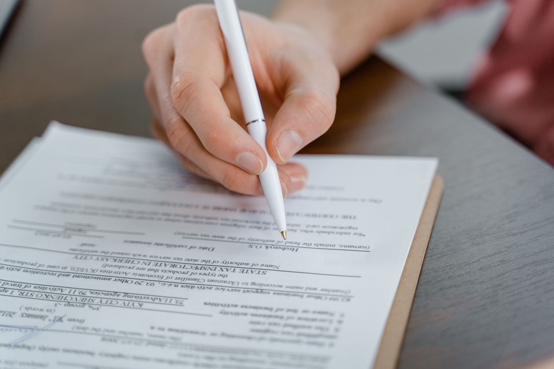 Offshore de pessoa física: quando vale a pena e os custos A hand holding a pen signing a document, close-up shot with focus on the paper.