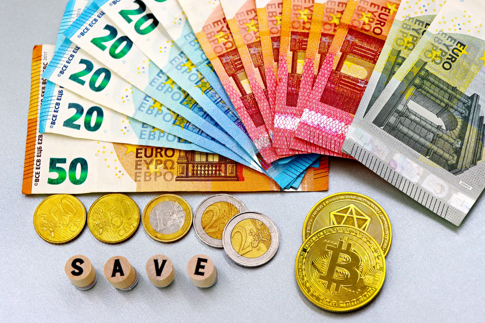 É possível usar Pix para comprar euros? Entenda o processo Euro banknotes and cryptocurrency coins arranged on a white surface with blocks spelling 'SAVE'.