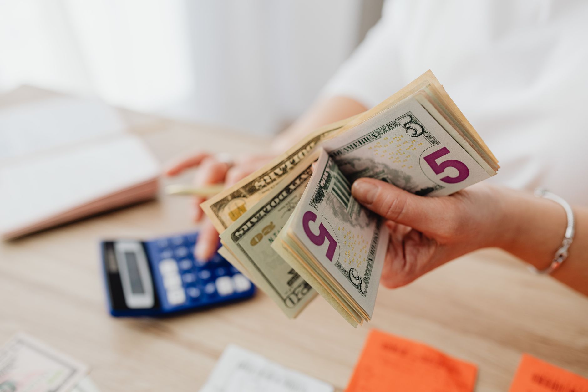 Por Que o Dólar Sobe Quando o Fed Aumenta os Juros Close-up of hands counting US dollar bills with a calculator, highlighting finance and savings.