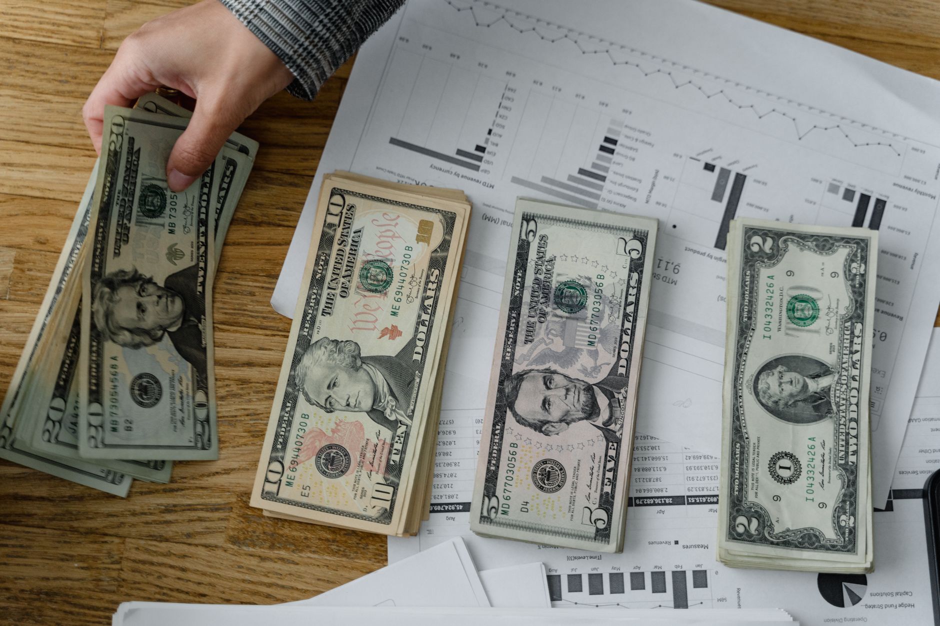 Notas de euro e de dolar americano dispostas lado a lado sobre uma mesa de madeira.