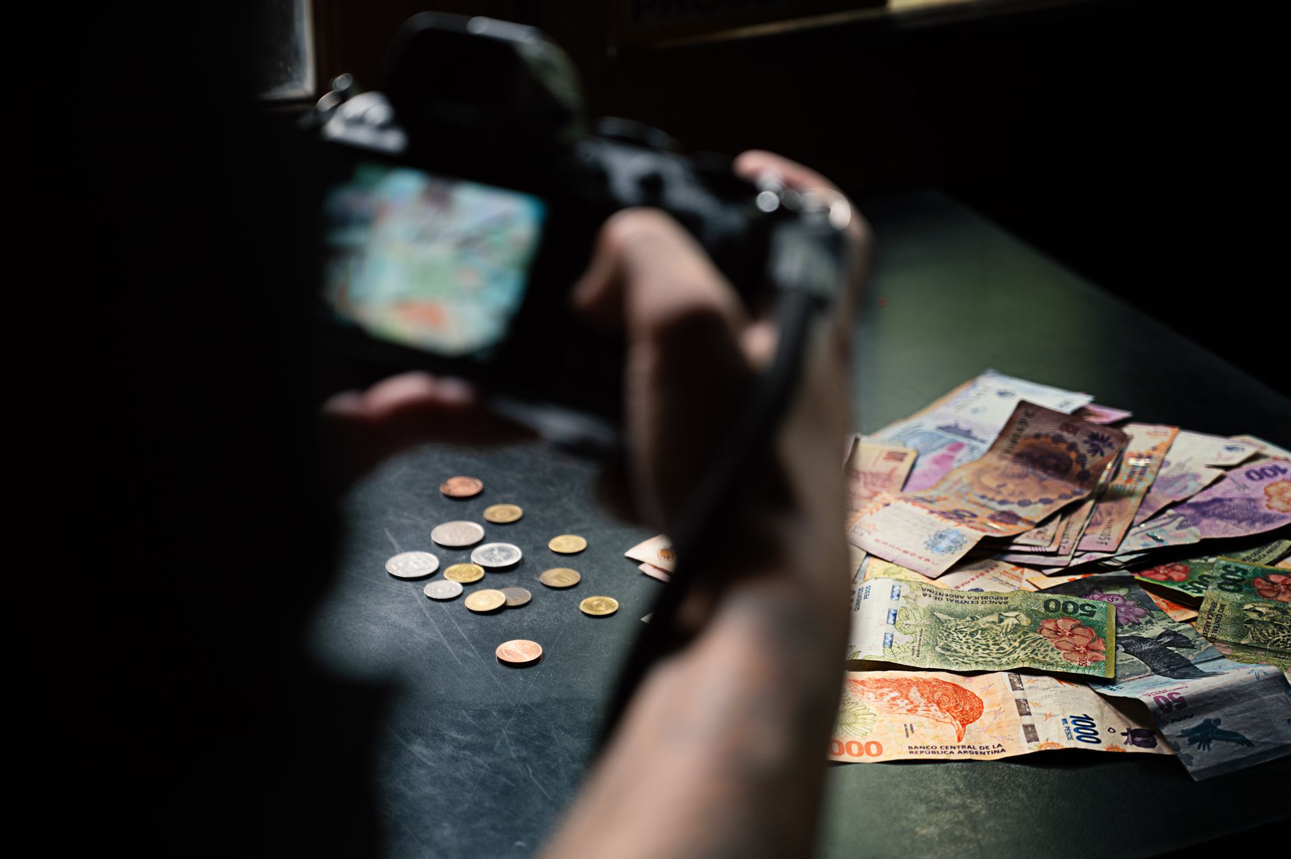 Pessoa analisando contas e uma tela com cotação de moedas em uma mesa