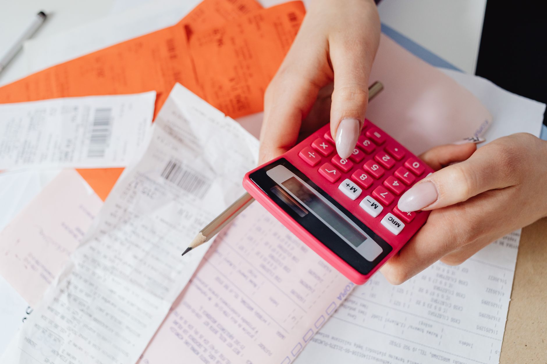 Por que o real é uma moeda volátil Hands using a pink calculator to manage expenses amidst various receipts and documents.