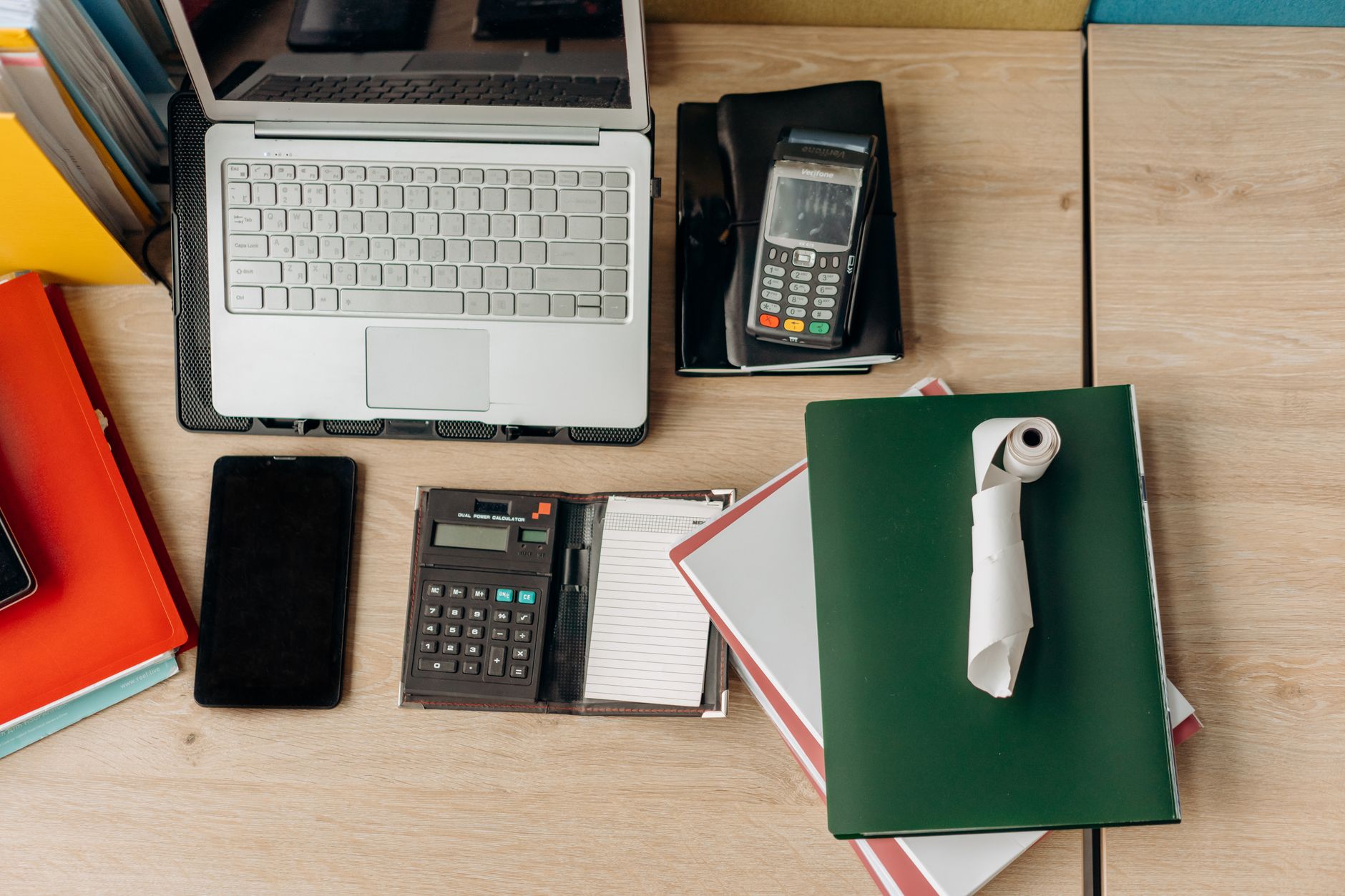 O que é a PTAX do euro? An organized office desk featuring a laptop, calculator, payment terminal, and documents.