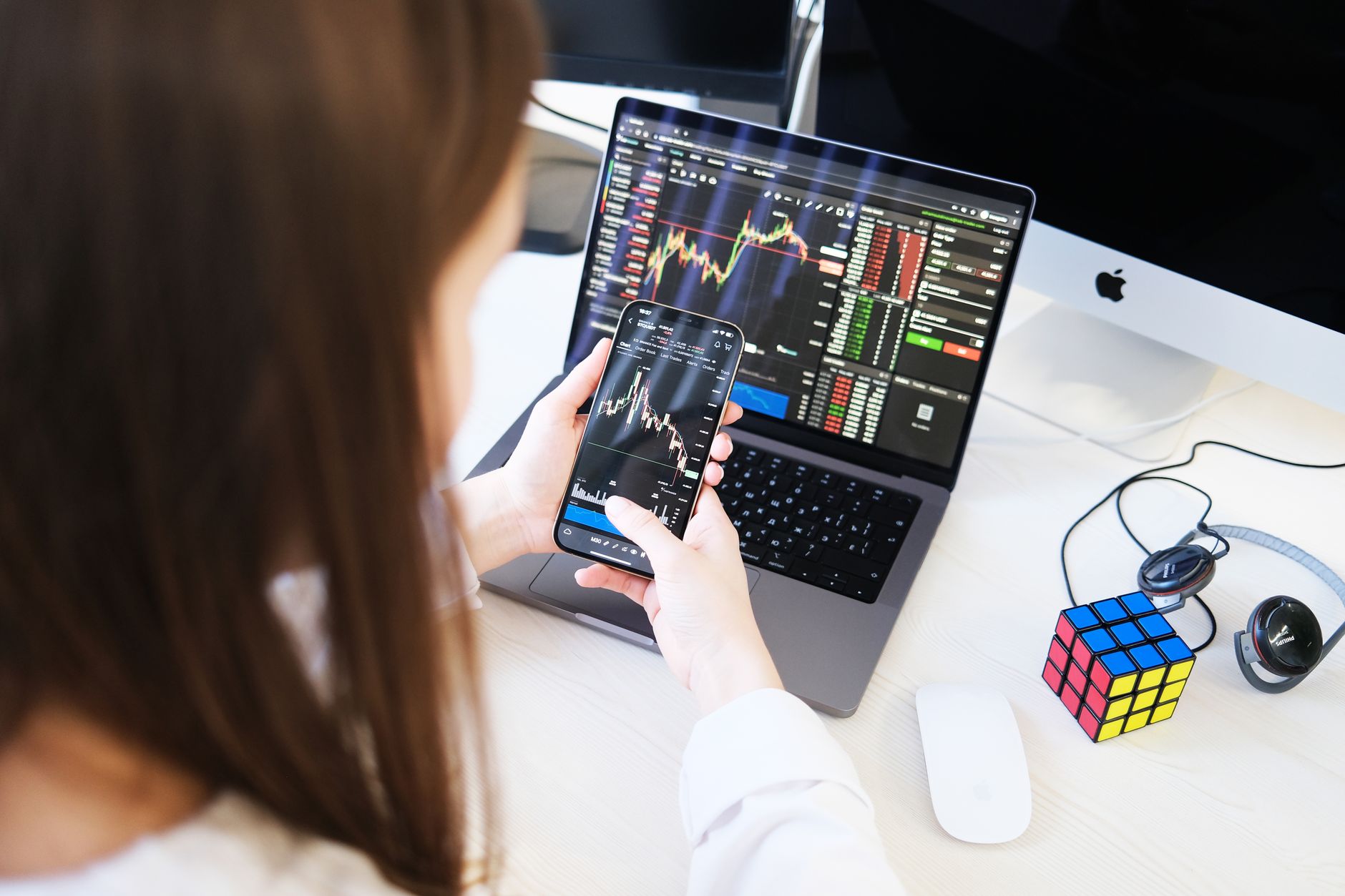 A woman trading cryptocurrency with charts on a smartphone and laptop, showcasing digital finance technology.