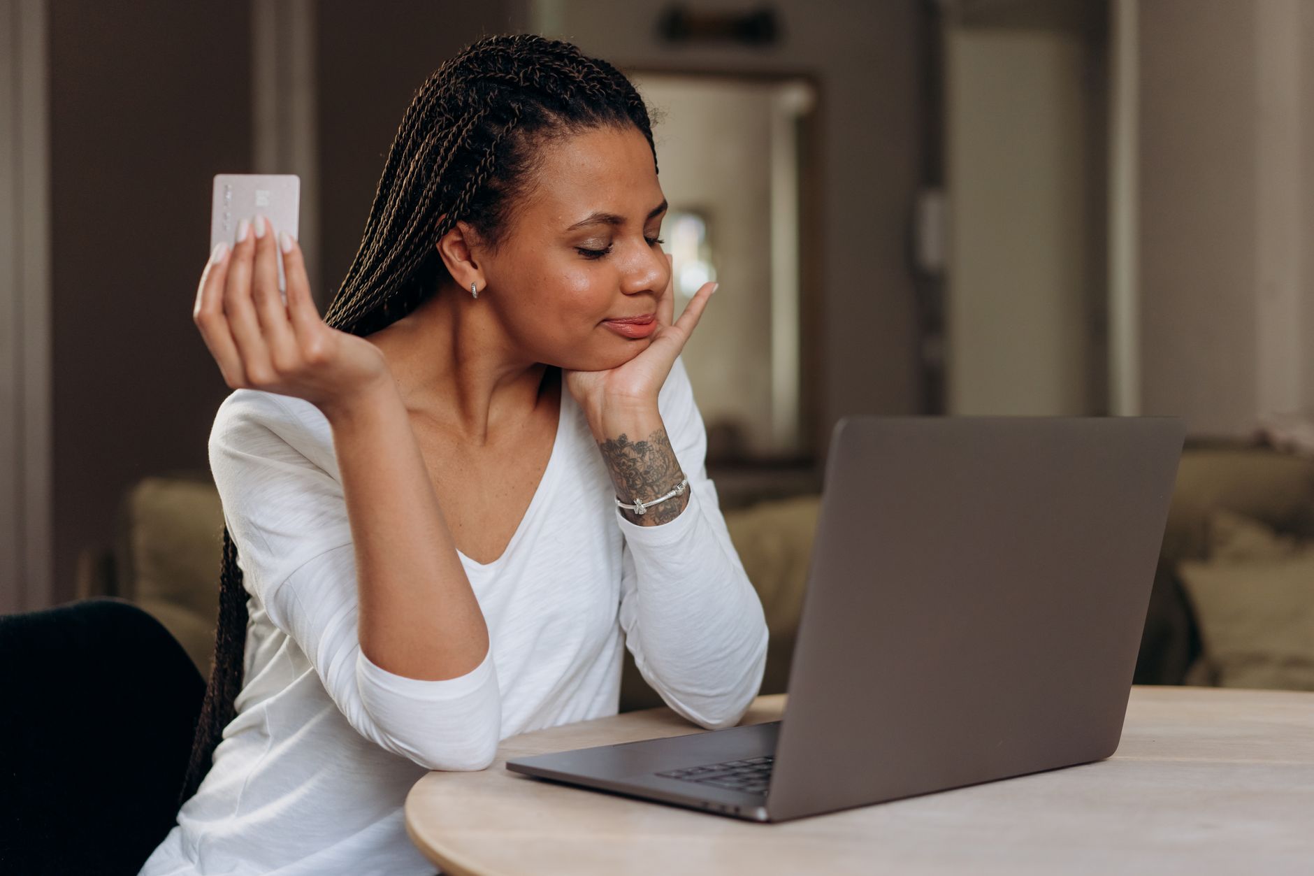 Quais lojas online aceitam cartão internacional brasileiro A woman enjoys shopping online, holding a credit card next to her laptop at home.