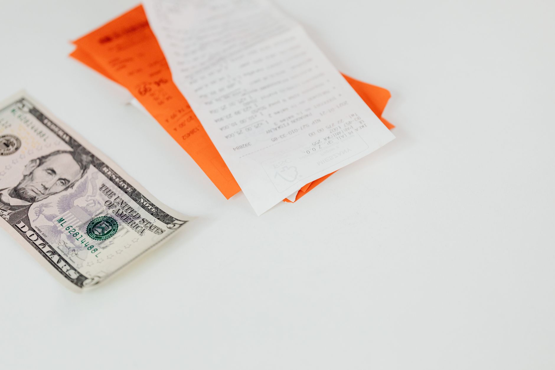 Qual o melhor horário do dia para comprar dólar A five dollar bill and receipts on a white surface, emphasizing finance and expenses.