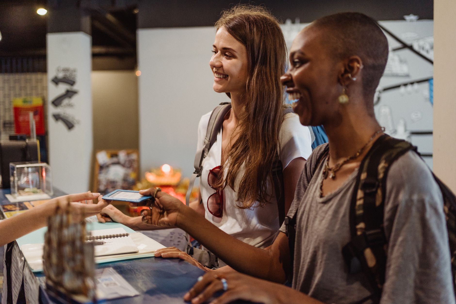 Qual o melhor lugar para trocar euro no Brasil Two women enjoying a cheerful check-in at a hostel reception desk.