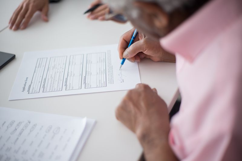 Elderly man signing important business document at desk in office setting.