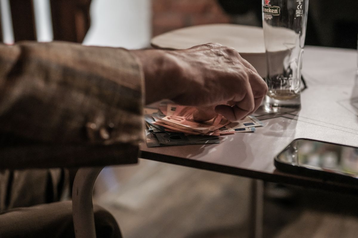 Mão segurando uma nota de euro e moedas sobre uma mesa de café na Europa