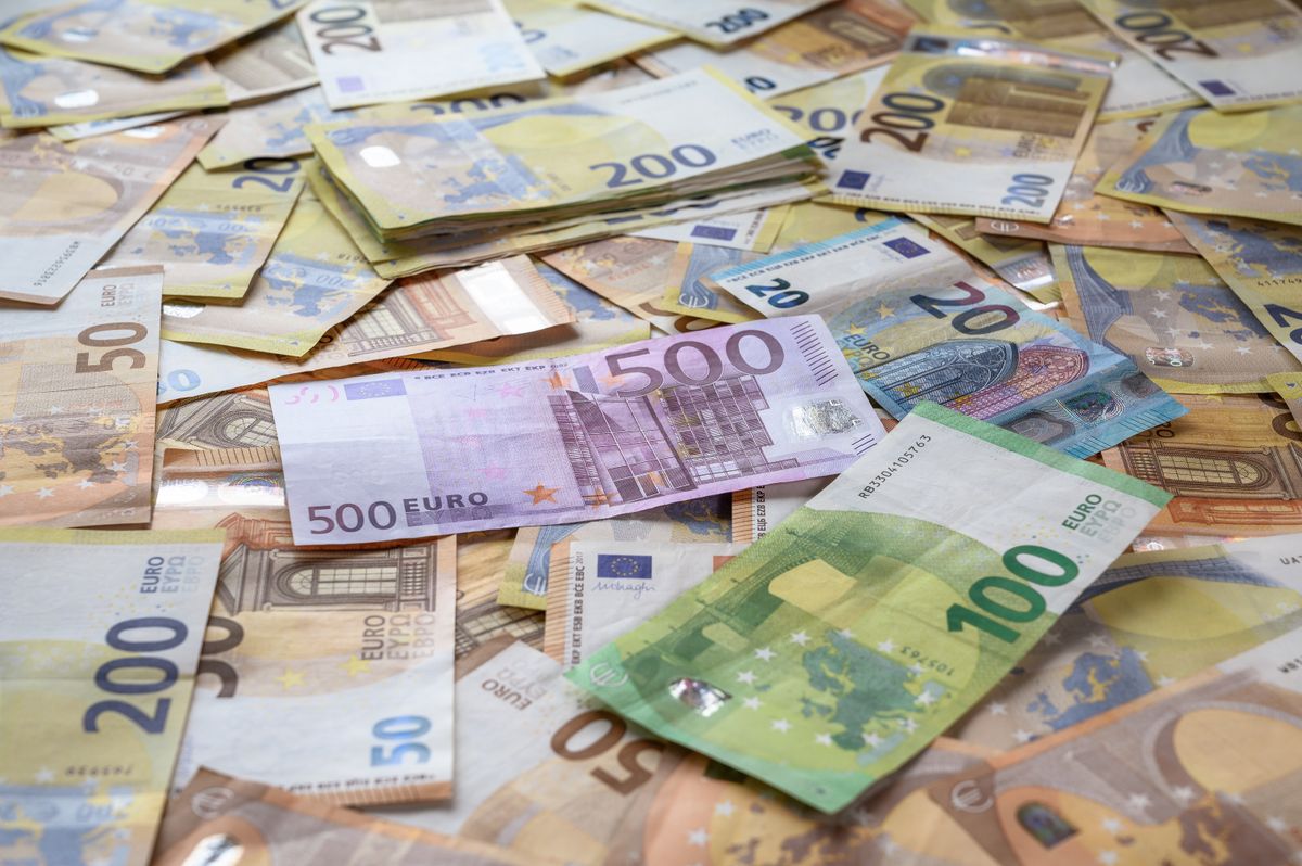 Notas de euro e cédulas de real sobre uma mesa de madeira ao lado de um passaporte.