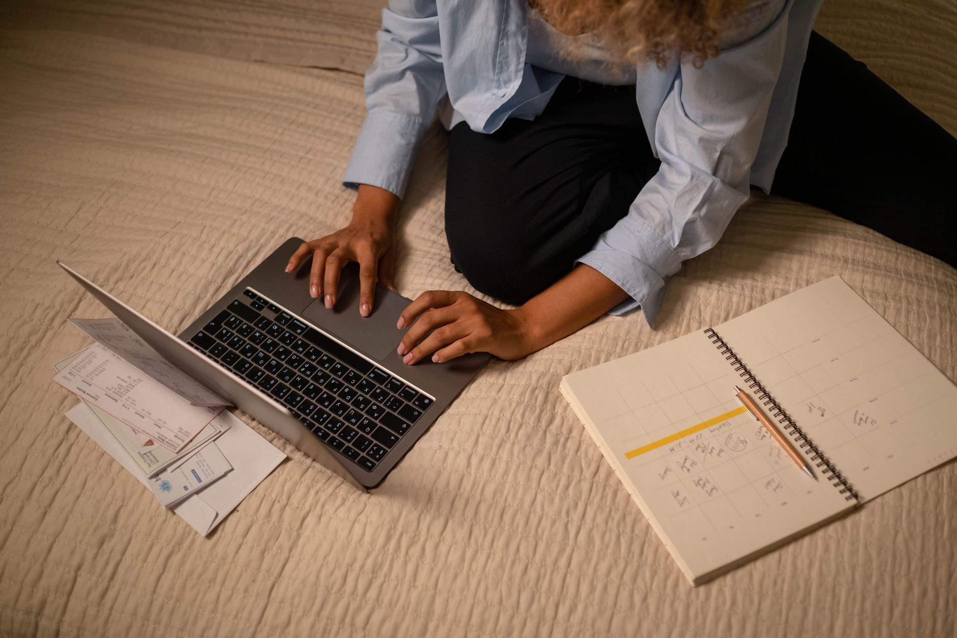 Como receber renda em euro? Veja as alternativas A woman working on a laptop while planning and organizing notes on a bed.