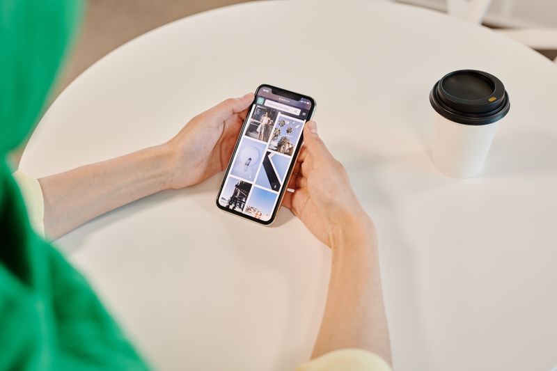 Reserva de emergência em euro: como montar para morar fora Close-up of hands holding smartphone browsing images with coffee cup on table.