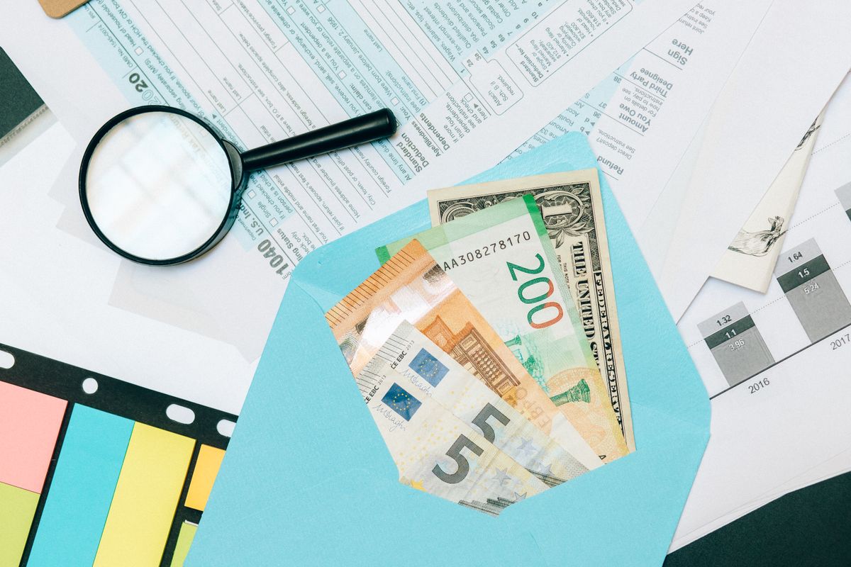Pessoa analisando notas de euro e dólar sobre uma mesa de planejamento financeiro