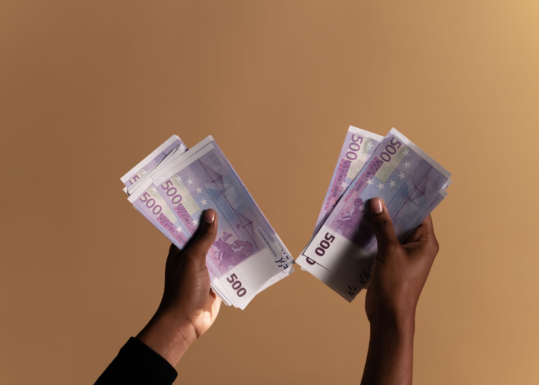 Receber salário em euro: como funciona e obrigações Close-up image of hands holding 500 euro banknotes on a neutral beige background.