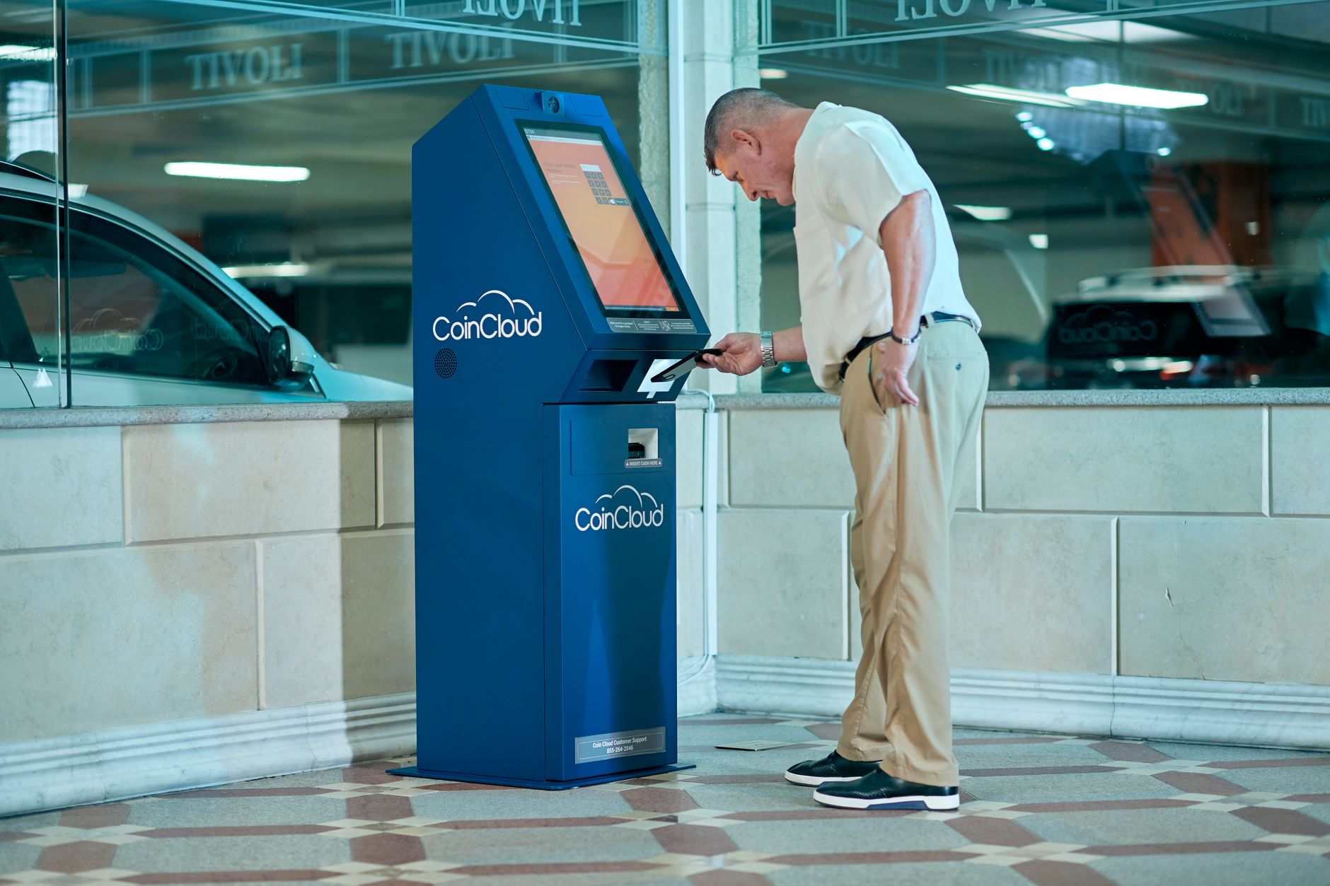 Como sacar euros durante uma viagem à Europa de forma eficiente Man interacting with a blue Coin Cloud machine indoors, illustrating modern finance technology.