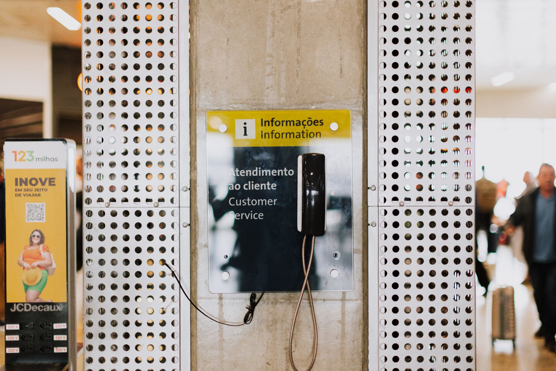 Public phone for customer service at a bustling station entrance with signage.
