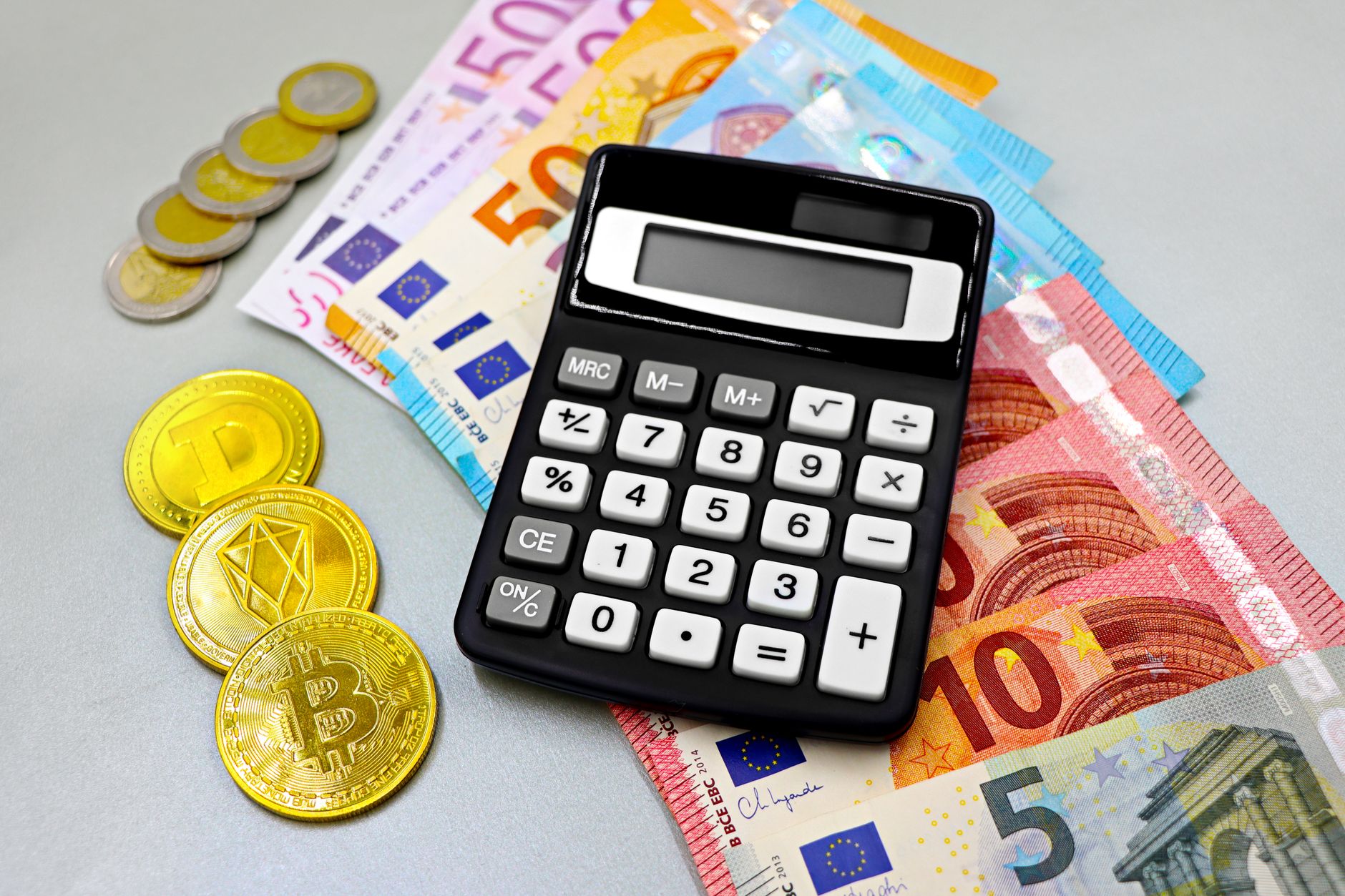 Pessoa segurando moedas de euro e calculadora sobre mesa de madeira