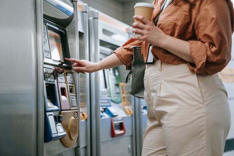 Transporte público na Europa: como planejar os gastos em euros Woman purchasing subway ticket from a machine, holding a coffee cup.