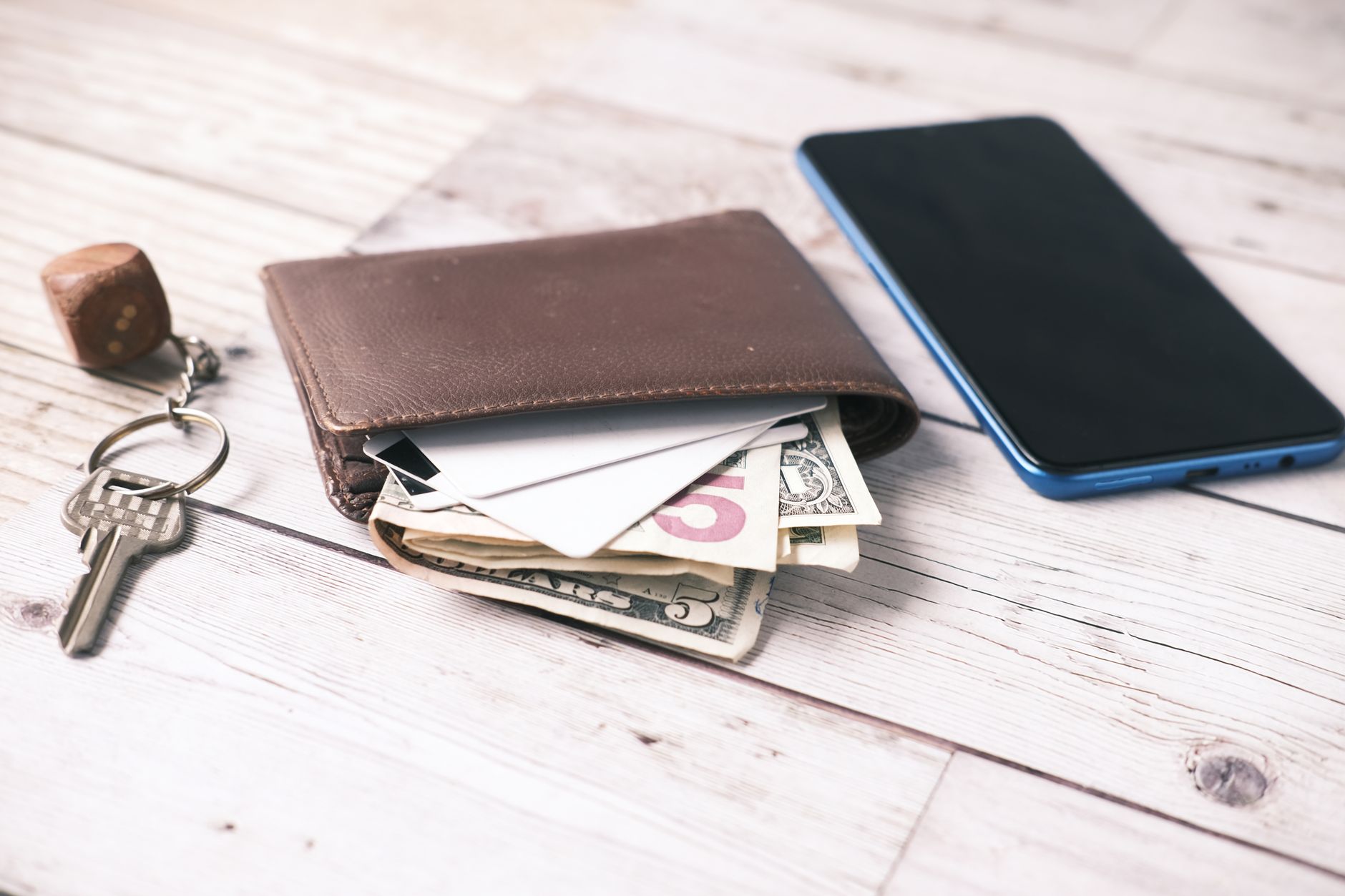 É possível trocar reais por euros na Europa? Close-up of a wallet with cash, smartphone, and keys on a wooden surface.
