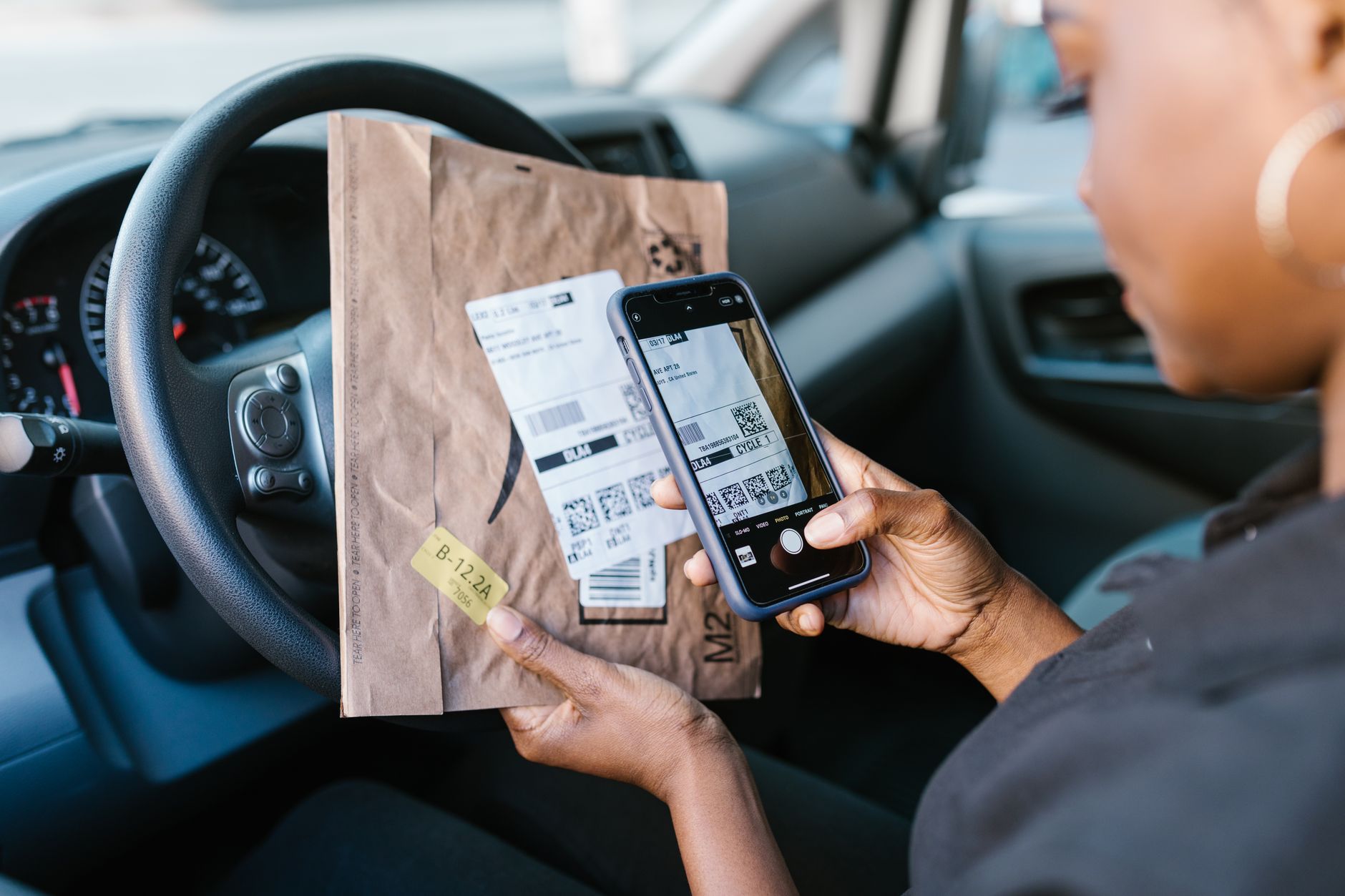 Consultar NF-e no portal da Sefaz: o que aparece Close-up of a courier in a car scanning a package label with a smartphone for delivery service.