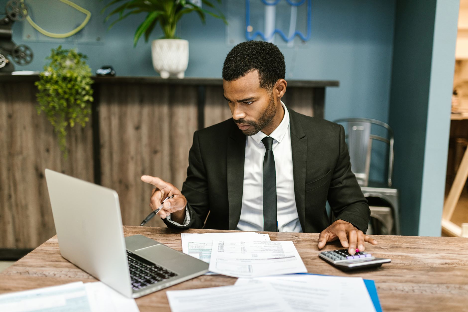 O que é IVA e como funciona no Brasil Professional man in a suit using a laptop and calculator in an office setting.