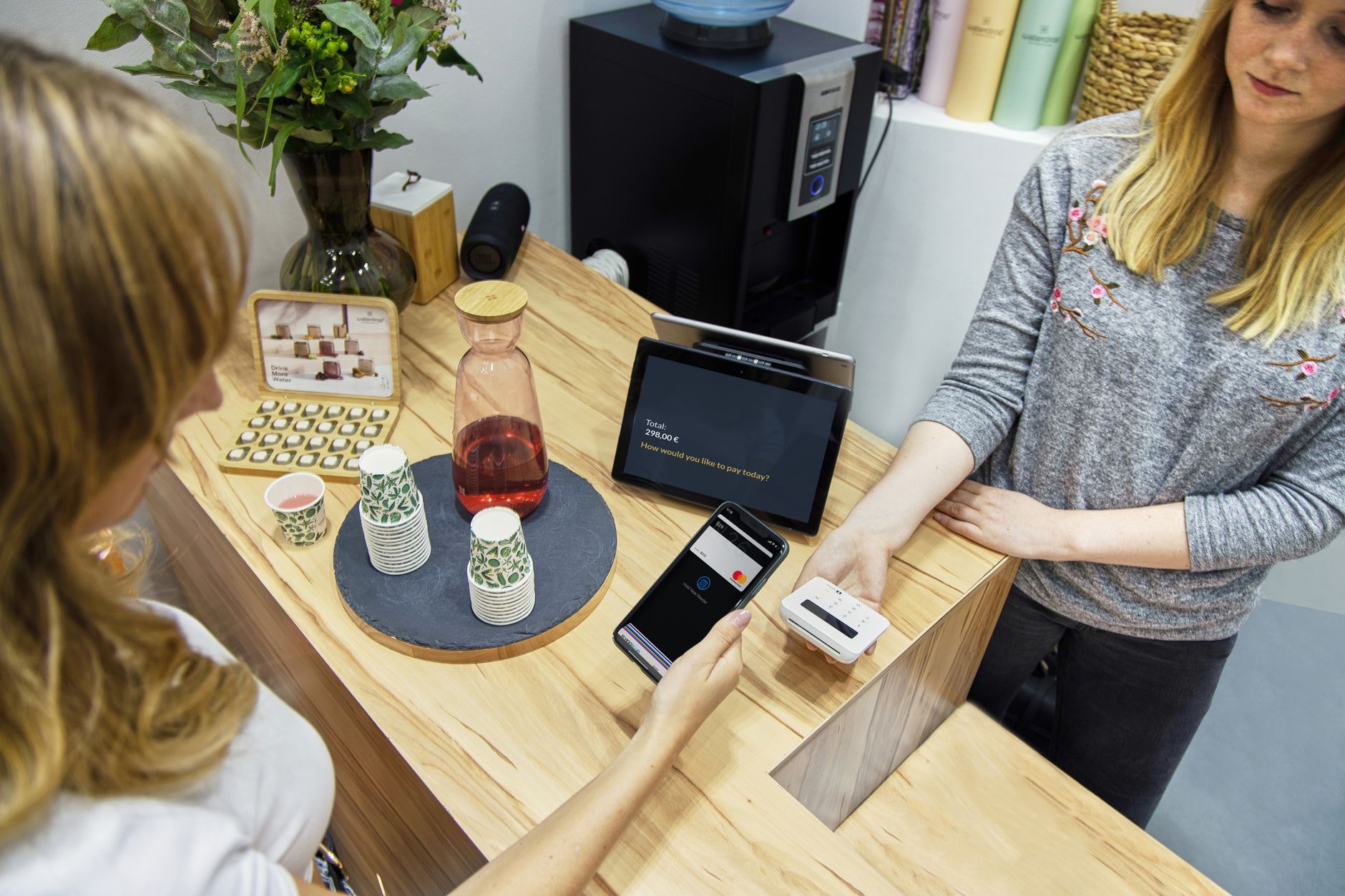 NFC-e: o que é e quando usar no lugar da NF-e A woman makes a contactless payment at a stylish Berlin café, emphasizing technology and modern retail.