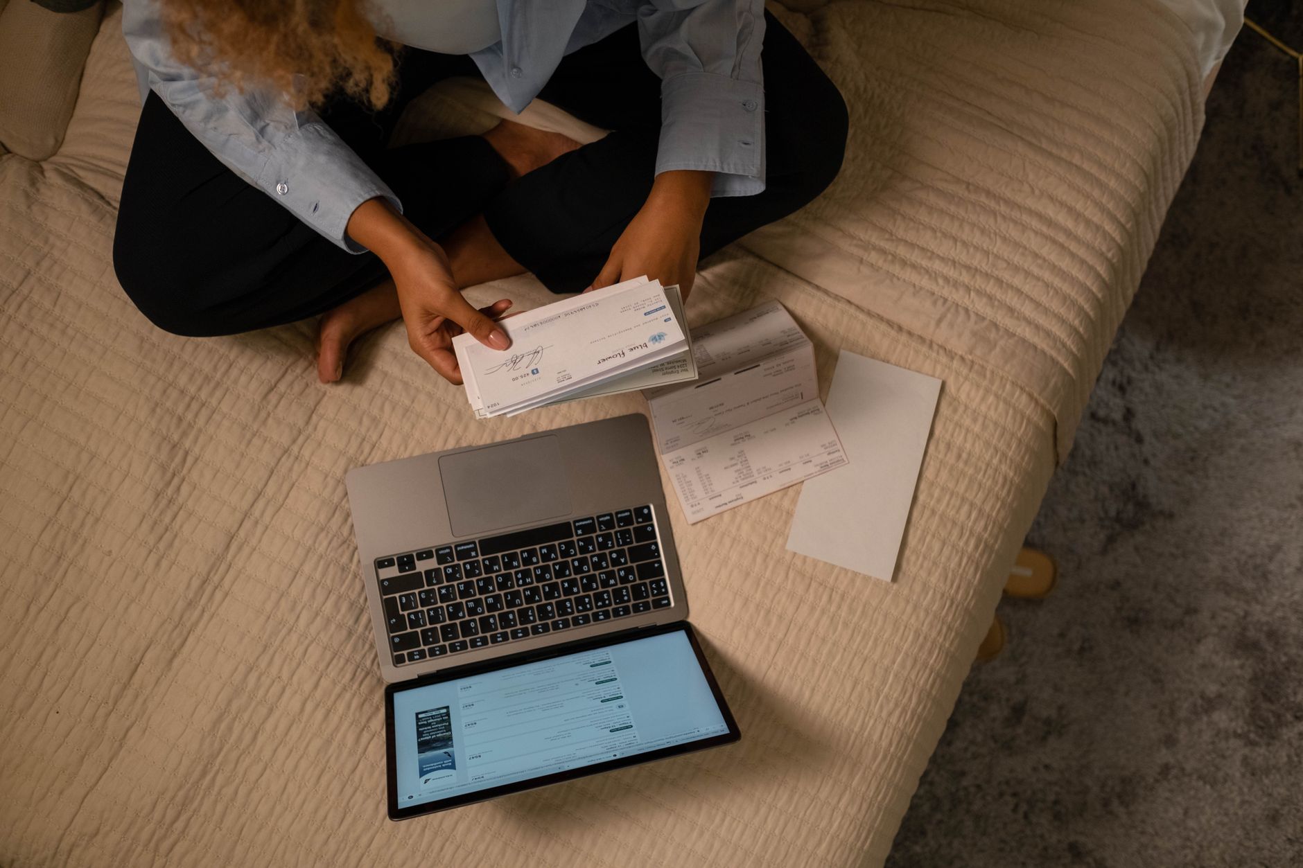 gov.br e NFS-e: como entrar e emitir sua nota Overhead view of woman organizing finances on bed with laptop and checks.